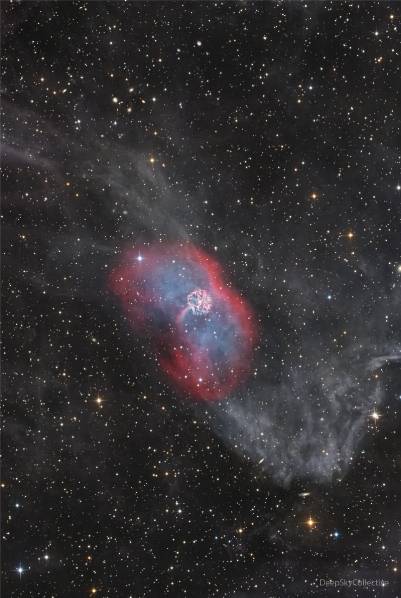 A faint nebula runs vertically in the image. In thecenter is a red envelope surrounding diffuse blue emission.In the center is a bright multicolored nebula that is nearly circular. Please see the explanation for more detailed information.