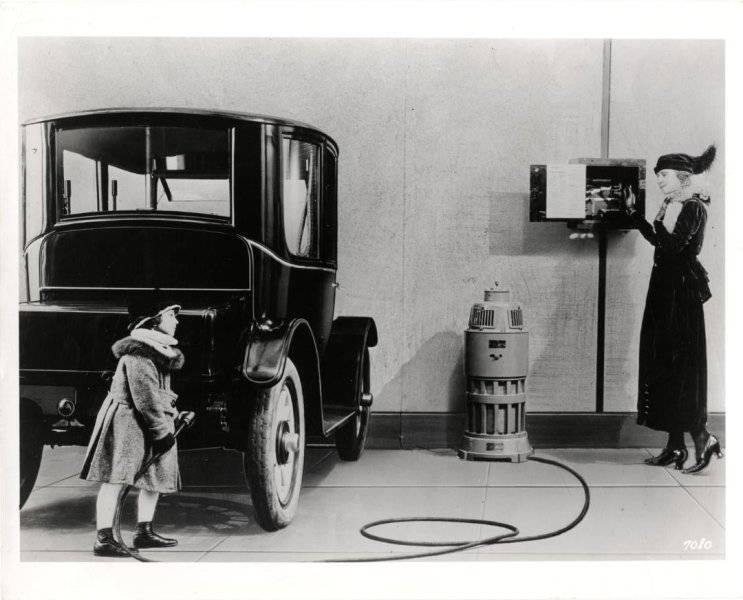 View of a girl charging a Baker electric car, while a woman stands next to a wall-mounted elec...jpg