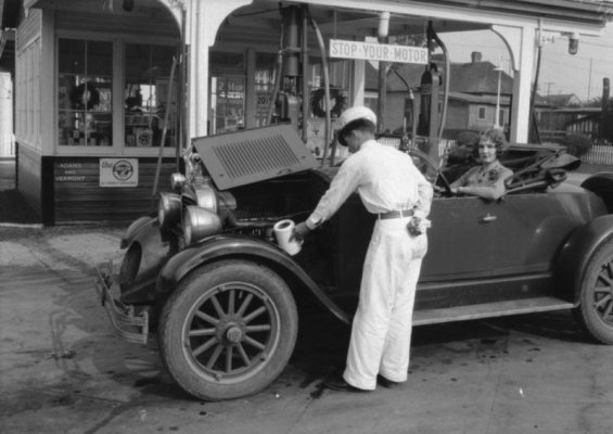 An attendant topping off the oil of a young lady's car at a Standard Gas Station on the corner...jpg